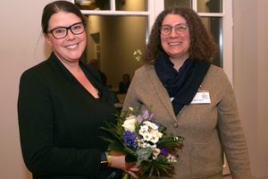 Zwei Frauen lächeln in die Kamera, die jüngere hält einen Blumenstrauß in der Hand